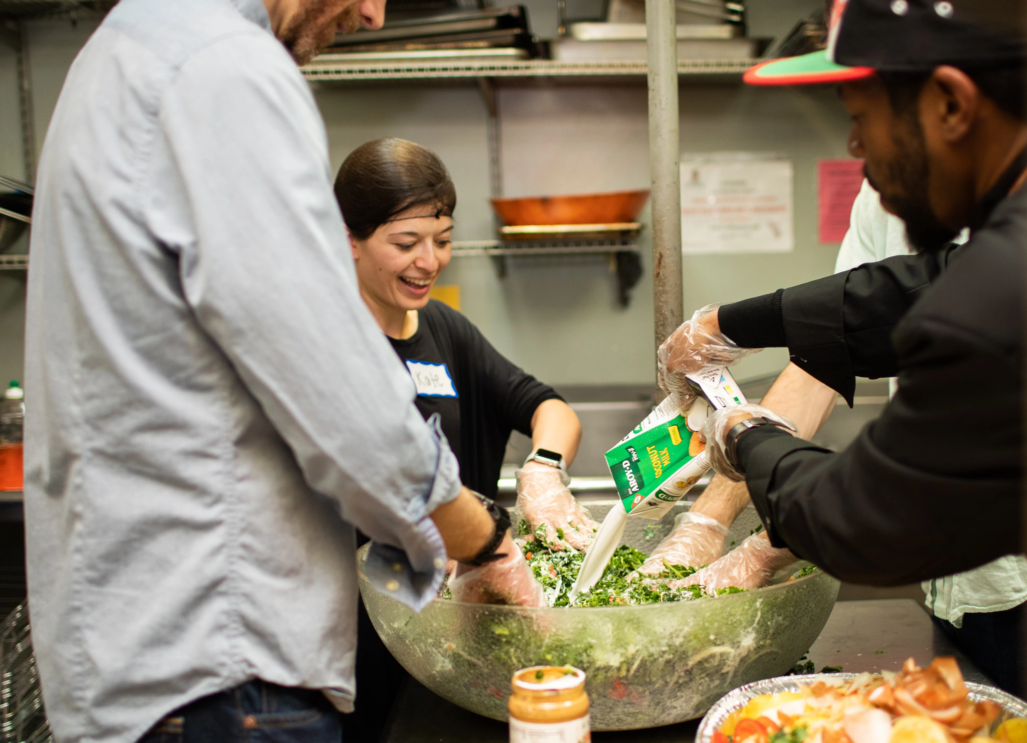 Three Repair the World volunteers prepare food collaboratively in an industrial kitchen
