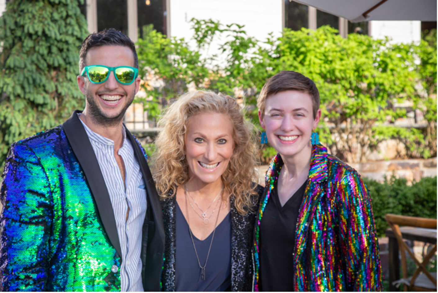Three staff members stand together smiling while dressed in sparkly outfits.