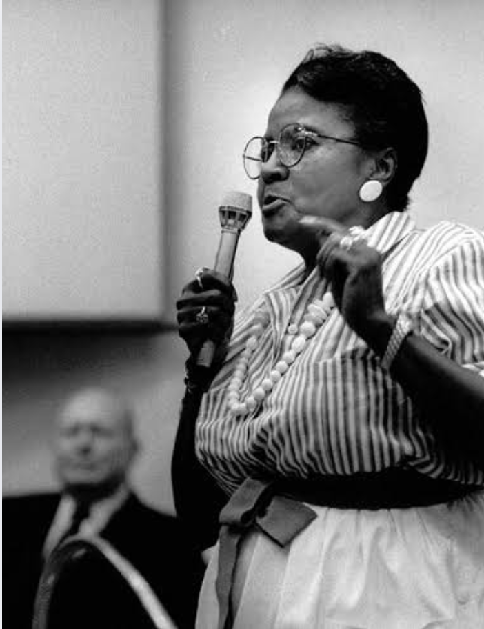 A black and white portrait of Dorothy Bolden holding a microphone and speaking to an audience.