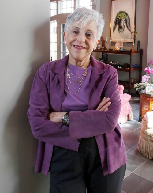 Lynn Schusterman wearing purple top and jacket smiling with arms crossed.